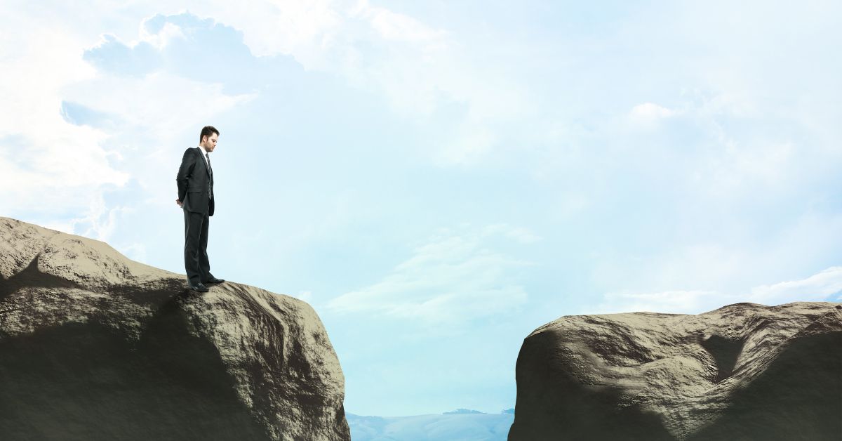 Overcoming Contractor Skill Gaps: A man standing at the edge of a cliff looks at the chasm between his cliff and another nearby cliff.