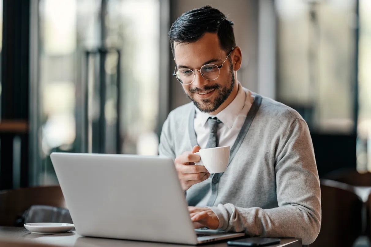 Male Holding Cup While Browsing On Laptop
