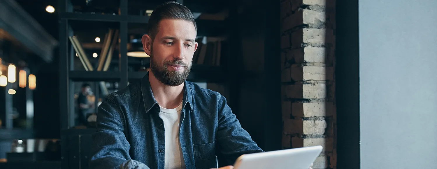 Young Adult Sitting In Cafe Working With Laptop